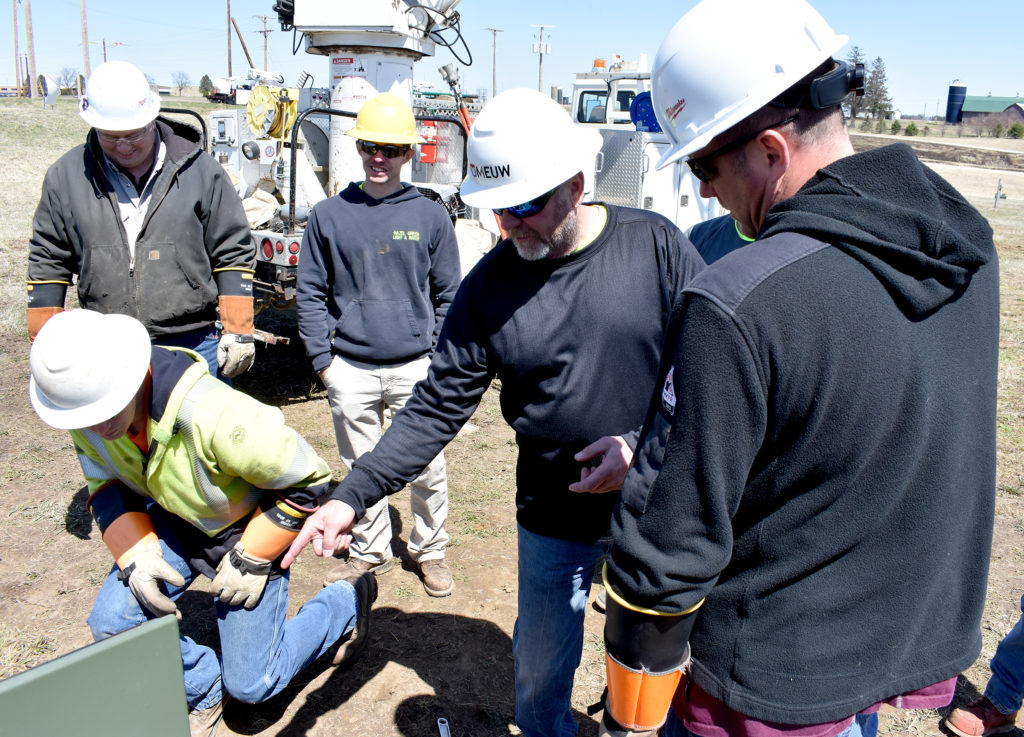 Instructor leads students in electrical training near green electrical box.