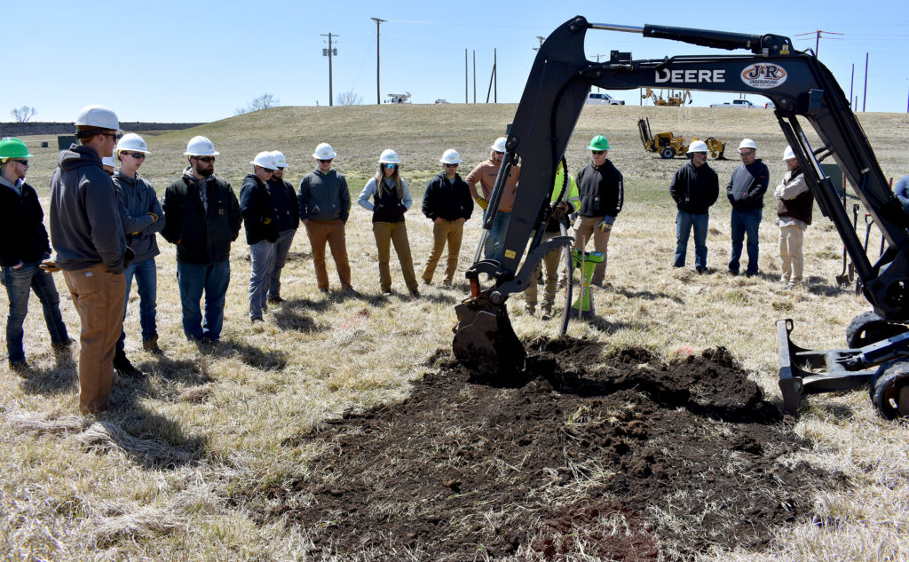 Students in hardhats standing as a hole is dug.