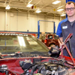 Male student standing next to vehicle with no hood.