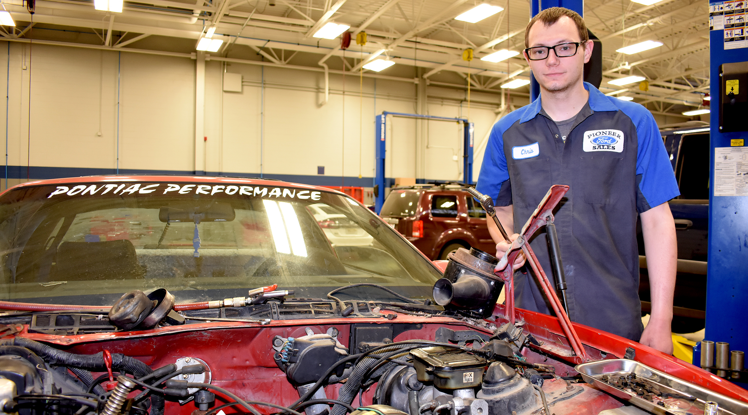 Male student standing next to vehicle with no hood.