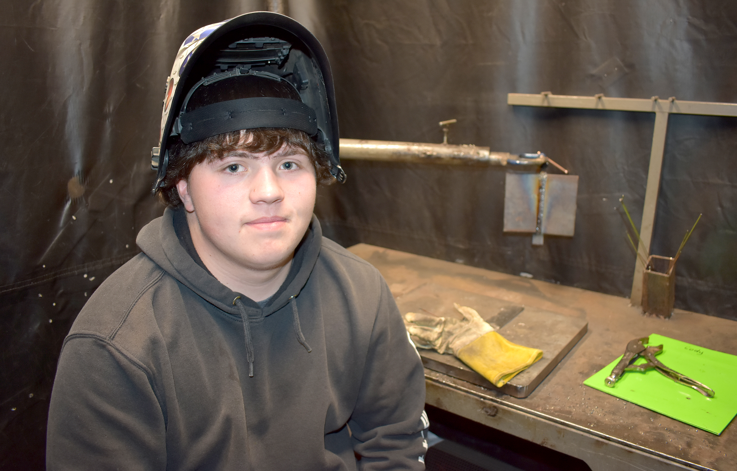 Male student sitting, wearing welding helmet.
