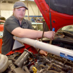 Male student next to vehicle with open hood.