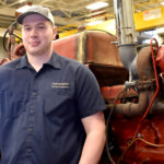 Male ag student standing in front of older red tractor.