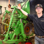 Male ag student standing in front of green machinery.