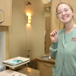 Dental student smiling at work, holding work instrument.