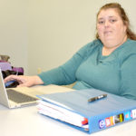 Female student sitting behind desk, laptop on desk.