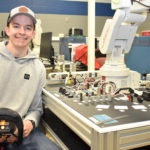 Male student sitting next to mechanical robotic controls.