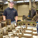 Male ag student standing behind engine parts.