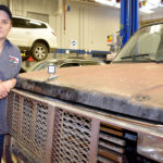 Male student standing next to truck hood.