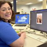 Female student sitting in front of computer and laptop on desk.
