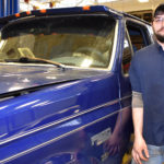 Male student standing in front of blue truck.