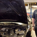 Male student standing next to vehicle with hood open.