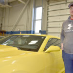 Mmale student standing next to yellow Camaro.