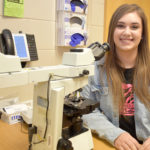 Female student sitting by microscope.