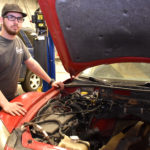 Male student next to vehicle with open hood.