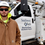 Lineman student standing in front of utility truck wearing white helmet.