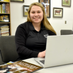 Female student sitting at desk with computer on table.