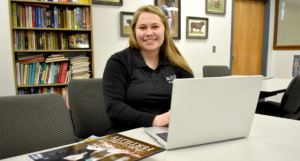 Female student sitting at desk with computer on table.