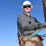 Male student wearing hard hat on electrical pole.