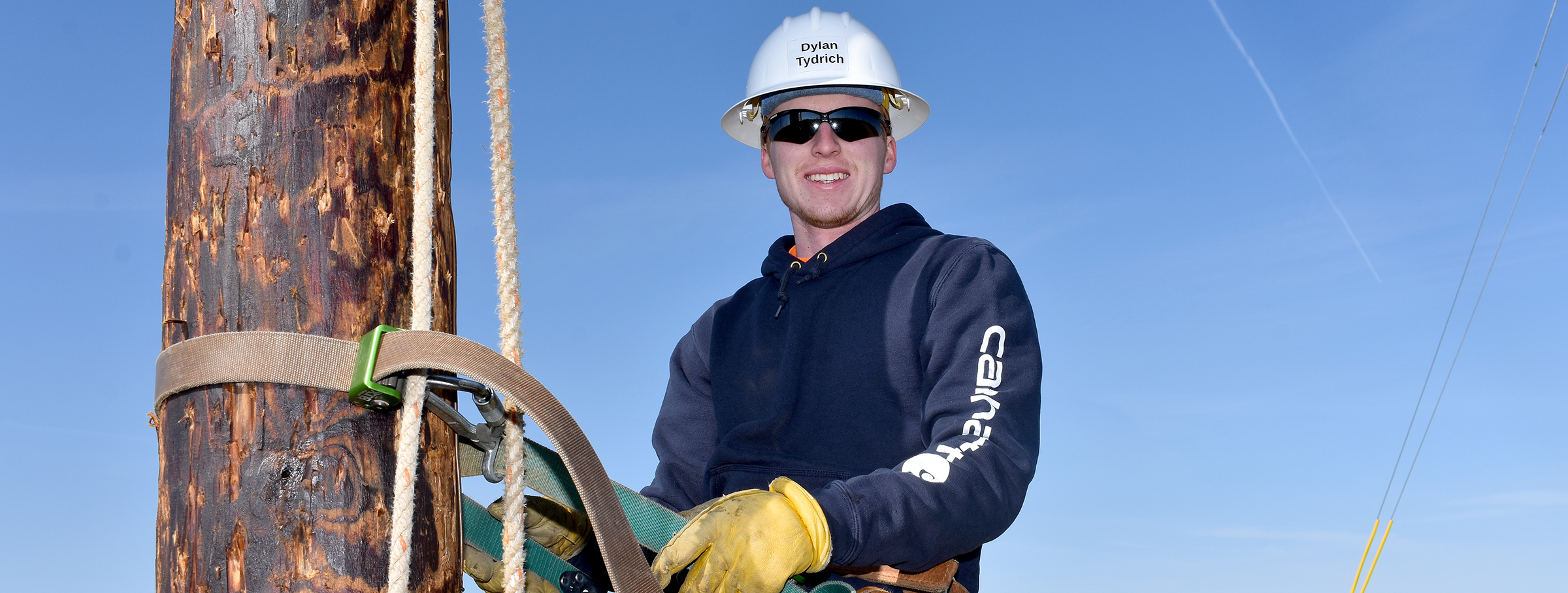 Male student with hardhat on electrical pole.