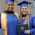 Two females graduates in blue caps and gowns smiling at camera