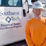 Male student wearing hard hat in front of utility truck.