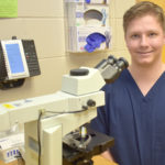 Male student sitting next to microscope.
