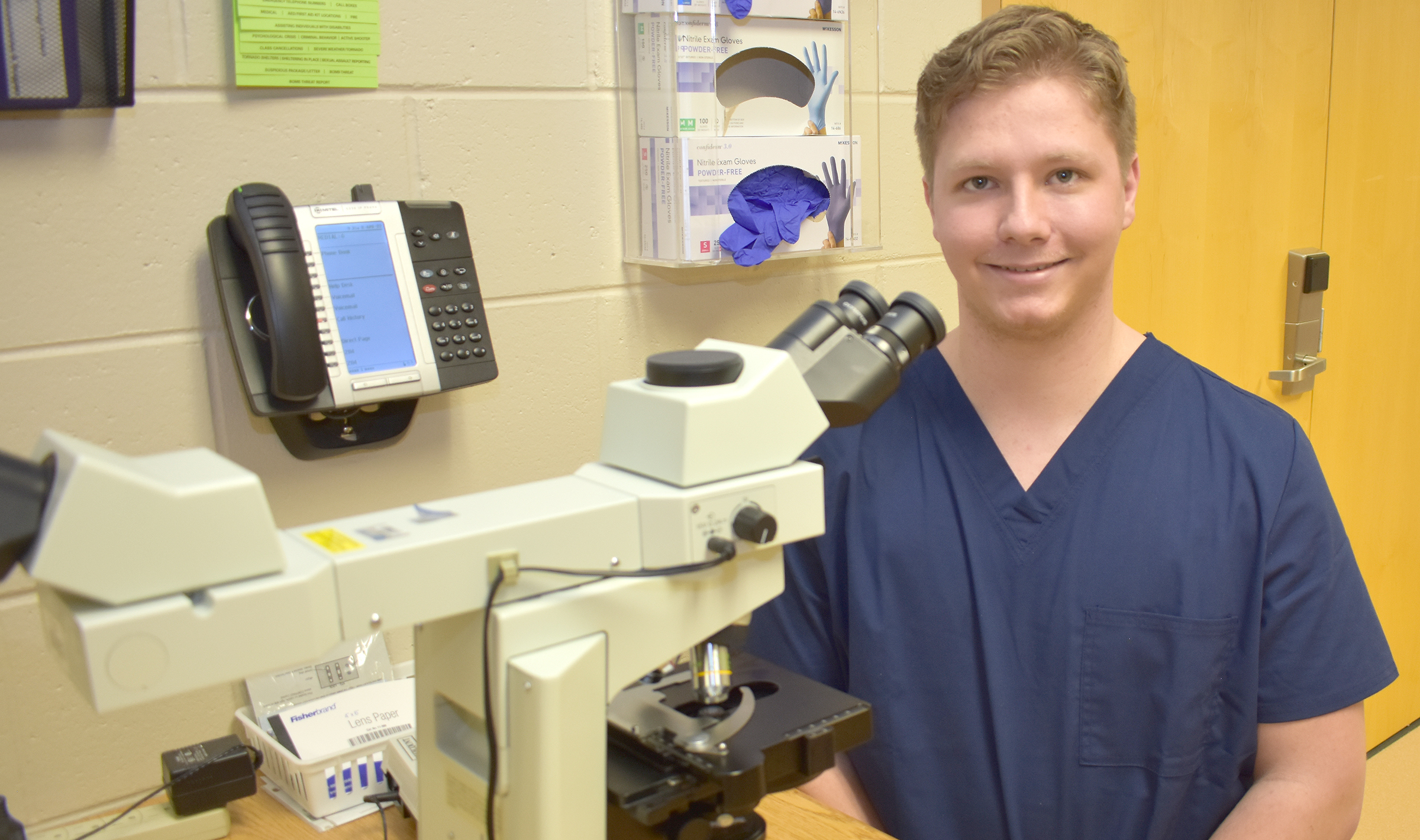 Male student sitting next to microscope.