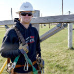 Male student wearing hard hat next to electrical equipment.