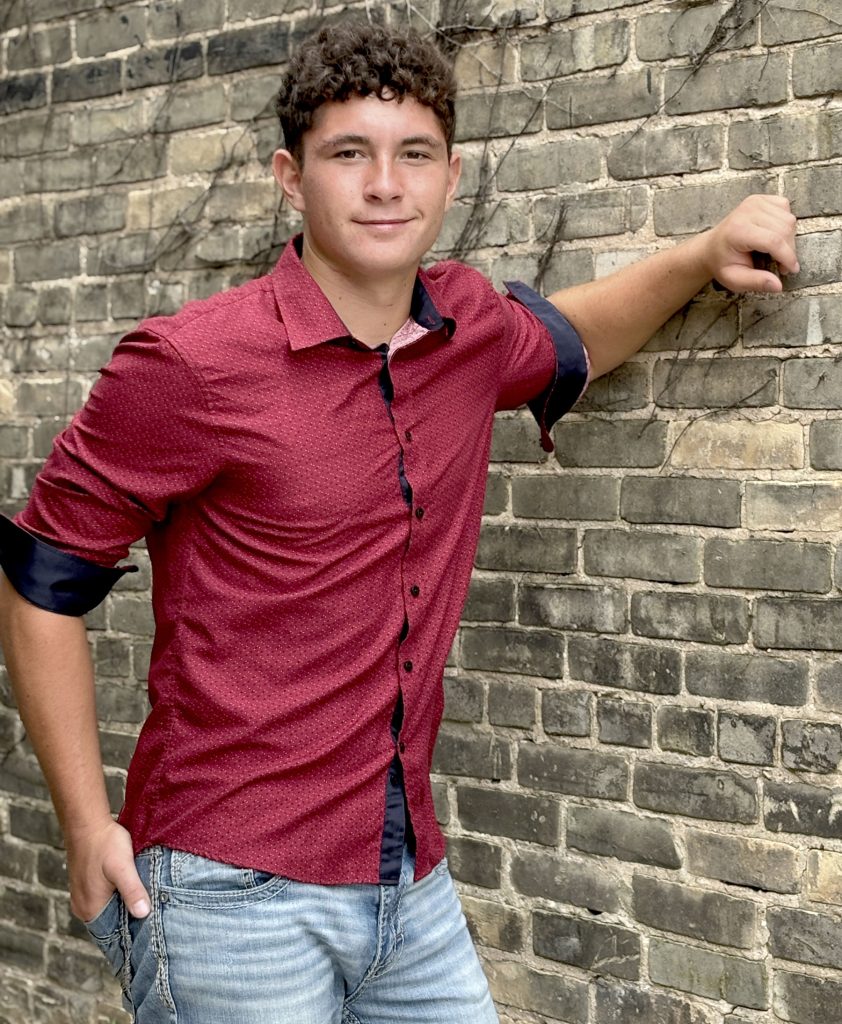 Hewsten, wearing a red shirt, leaning against a brick wall.