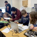 Middle school students in classroom, working on machines.