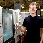 Cody holding a metal cube in front of a CNC machine.