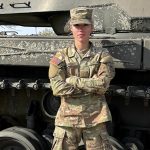 Lizzy in her Army uniform standing next to a tank.