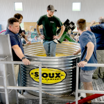 Man standing in grain bin, surrounded by other men.